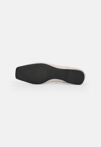 Suela de zapato de color claro con una superficie texturizada. Presenta una base de goma negra sólida y un diseño elegante y aerodinámico.