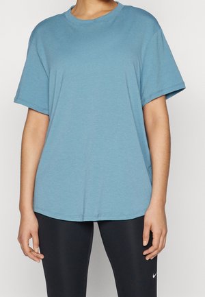 Osoba nosząca luźną niebieską koszulkę i czarne legginsy sportowe z małym białym logo Nike na lewej nodze.