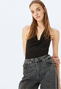 Body nera senza maniche con scollo drappeggiato abbinato a jeans in denim grigio a vita alta con dettagli in contrasti argentati.