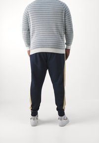 Ljusblå och vit randig tröja med ribbade ärmslut, ihop med marinblå träningsbyxor med en beige sidostripe, bärs med vita sneakers.