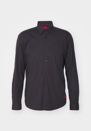 Camisa negra de manga larga hecha de algodón, con cuello tipo punta, botonadura frontal y un acento rojo en el interior del cuello. Tejido texturizado sin patrones.