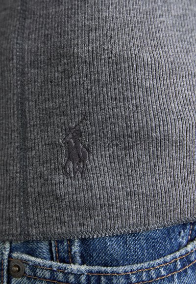 Grå ribbestrikket t-skjorte med mørk brodert logo. Kjennetegn inkluderer rett kant og strukturert overflate, sammen med blå denimjeans.