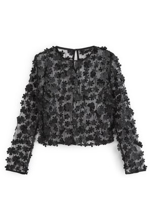 Blouse noire transparente ornée d'appliqués floraux, à manches longues, col rond, et design court avec une fermeture par bouton au dos.