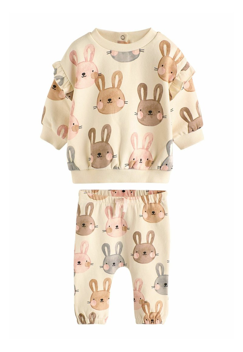 Krmovo bílý dvoudílný outfit skládající se z topu s králičími vzory, volánkovými rukávy a kalhot s elastickým pasem s odpovídajícími vzory.