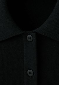 Tissu tricoté noir avec un col rabattable et deux boutons noirs visibles sur une patte de boutonnage verticale.