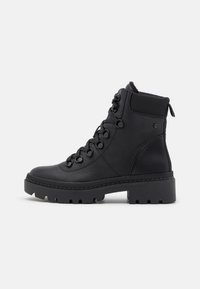 Bottine en cuir noir avec semelle crantée épaisse, lacets à l'avant avec œillets métalliques, col rembourré et languette à l'arrière.