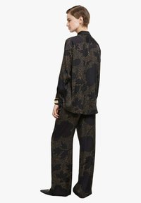 Completo nero con motivo a fantasia composto da una camicia a maniche lunghe con disegno floreale e pantaloni a gamba larga. Il materiale sembra liscio con una leggera lucentezza.