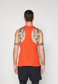 Orange mesh athletic tank top featuring a racerback design, with "NIKE TRAIL" text and large cutouts for ventilation. Black shorts.