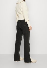 Black jeans with a high waist, straight cut, and lightly frayed hems, paired with a chunky cream knit sweater.