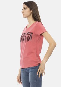 Roze katoenen t-shirt met een v-hals en korte mouwen, voorzien van gedurfde zwarte letters over de voorkant. Gemaakt met blauwe denim jeans.