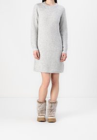 Abito grigio lavorato a maglia con maniche lunghe e texture a coste, abbinato a stivali in pelliccia sintetica beige con suola spessa.