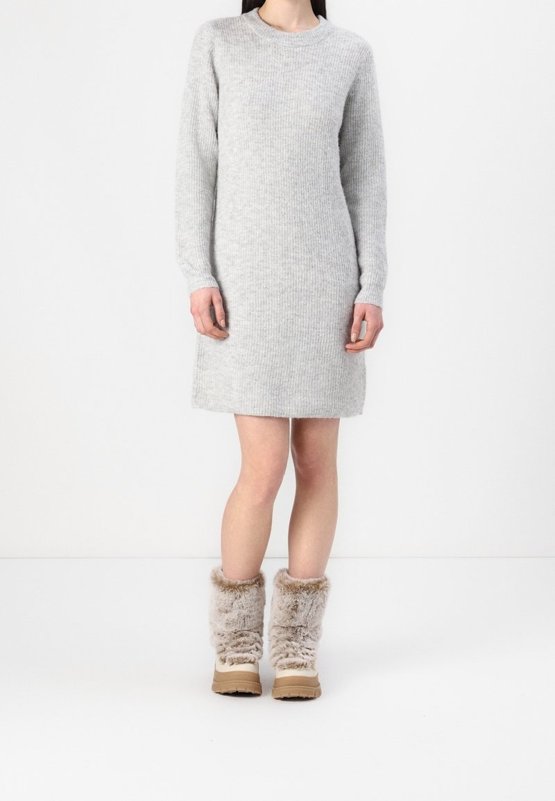 Abito grigio lavorato a maglia con maniche lunghe e texture a coste, abbinato a stivali in pelliccia sintetica beige con suola spessa.