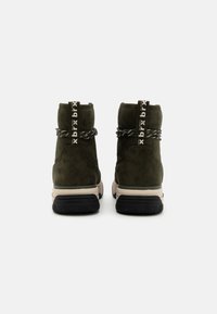 Bottes de cheville en daim vert avec une semelle en caoutchouc noir, présentant un lacet texturé enroulé et une languette avec un imprimé logo contrastant.