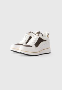 Hvite og brune kile-sneakers med gullakenter, snøring og tykk såle på en lys grå bakgrunn.