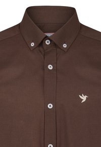 Camisa marrón de botones con cuello clásico, botones blancos y un logo de ave bordado en el pecho. Textura suave, diseño casual.