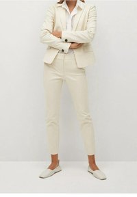 Completo beige composto da un blazer su misura con revers a punta, pantaloni slim-fit e ballerine di colore chiaro, il tutto in un tessuto dalla consistenza liscia.