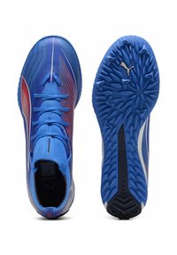 Zapatillas deportivas azules con una parte superior de malla texturizada que presenta acentos rojos, cordones planos y una suela de goma con patrón, mostrando el logotipo de Puma.