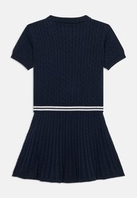 Μπλε σκούρο πλεκτό φόρεμα με ριγέ υφή, κοντά μανίκια και φούστα σε στυλ καμπάνα. Η λευκή ριγέ ζώνη προσθέτει λεπτομέρεια.