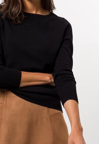 Zwarte gebreide top met lange mouwen en een ronde hals, gecombineerd met een tan suède rok, voorzien van een zijzak en een gladde afwerking.