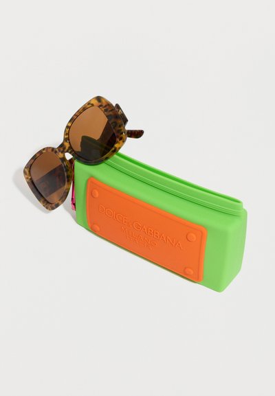Γυαλιά ηλίου με φολιδωτό σκελετό που ακουμπούν σε μια φωτεινή πράσινη ορθογώνια θήκη με πορτοκαλί λογότυπο Dolce & Gabbana Milano Italia.