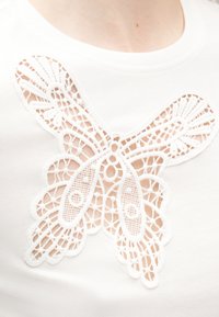 Gros plan sur un tissu blanc avec une découpe en dentelle détaillée en forme de papillon sur la poitrine supérieure d'une personne.