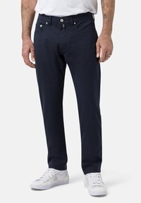 Marineblaue Baumwollhose mit geradem Schnitt, ausgestattet mit einem Knopf- und Reißverschluss, fünf Taschen und einer glatten Textur. Getragen mit weißen Sneakern.
