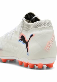 Puma FUTURE Fußballschuh, weißes Synthetik-Obermaterial mit strukturierter Gestaltung, schwarzes Logo, orangefarbene Akzente und mehrfarbige Stollen an der Sohle.