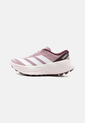 Vaaleanpunainen Adidas Terrex polkujuoksukenkä, jossa valkoiset raidat, paksu pohja ja nastallinen ulkopohja, kuvattuna sivuprofiilista.