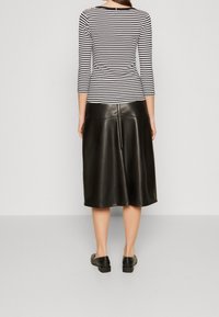 Musta tekonahkainen midihame, jossa on sileä pinta ja takana vetoketju, yhdistettynä mustavalkoraidalliseen pitkänhihaiseen paitaan.