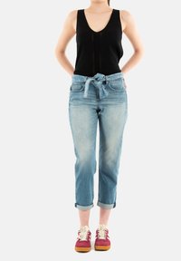 Top nero senza maniche, jeans in denim azzurro chiaro con cintura in vita, e sneakers bordeaux con lacci bianchi e suola marrone.