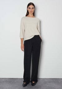 Hellbeige, gerippter Strickpullover mit Boot-Ausschnitt, kombiniert mit hochtaillierten, locker sitzenden schwarzen Hosen und spitzen schwarzen Schuhen.