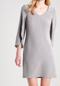 Grå skiftklänning med V-ringning och trekvartslånga ärmar, tillverkad av slät tyg med en enkel, ren silhuett. Inga utsmyckningar.