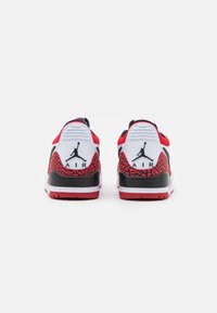 Zapatilla roja y blanca con una suela negra, que presenta un patrón texturizado en rojo y negro en el talón, y un destacado logo "Air".