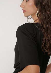 Czarna bluzka z krótkim rękawem o dopasowanym kroju, wykonana z gładkiego, miękkiego materiału, z okrągłym dekoltem i rękawami o długości do łokcia.