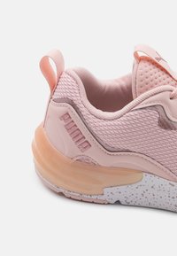 Rosa sneaker med ett texturerat mesh-överdel, en dämpad sula med fläckig detaljering och en framträdande logotyp på sidan.