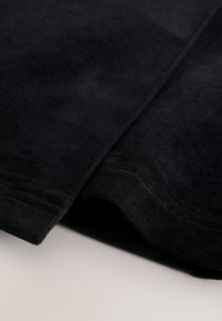 Gros plan sur un tissu en velours côtelé noir montrant une texture côtelée et des bords pliés sur un fond clair.