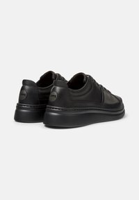 Zwarte leren schoenen met een gladde afwerking, met ronde neuzen en dikke zolen, weergegeven vanuit een achteraanzicht dat het ontwerp en het merkembleem benadrukt.