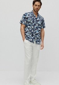 Korte mouwen button-up shirt in marineblauw met wit bloemenpatroon, gecombineerd met lichtbeige linnen broek en witte sneakers.