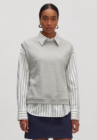 Grauer Sweatshirt mit hohem Kragen und kurzen Ärmeln, über ein weißes gestreiftes Hemd mit Kragen getragen. Glatter Stoff, lockere Passform.