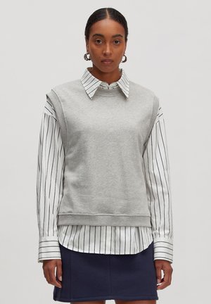 Grauer Sweatshirt mit hohem Kragen und kurzen Ärmeln, über ein weißes gestreiftes Hemd mit Kragen getragen. Glatter Stoff, lockere Passform.