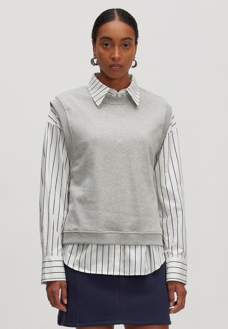 Grijze sweatshirt met hoge hals en korte mouwen, gelaagd over een witte gestreepte blouse met kraag. Glad materiaal, relaxed fit.