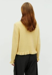 Világos sárga pulóver, cropped fazonnal, bordázott rojt betéttel az alján és az ujjakon, puha, texturált anyagból készült. A hátoldali nézet minimális részletezést mutat.