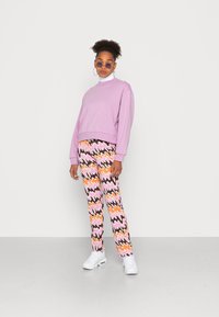 Sweatshirt oversized em lavanda, tecido leve; calças com padrão zigzag multicolorido em rosa, laranja e preto; ténis brancos.