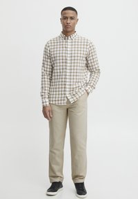 Brun og hvit rutete skjorte med knapper og lange ermer, kombinert med beige bukser og svarte sneakers. Enkel, skreddersydd design.