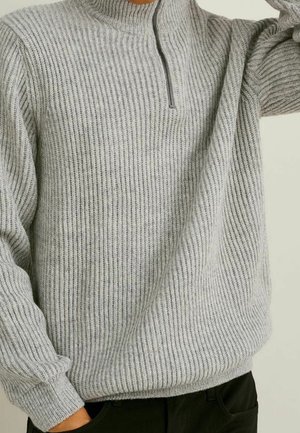 Jersey de color gris claro con textura en relieve, cuello alto y cierre de media cremallera. La tela texturizada presenta un patrón sutil y mangas ajustadas.