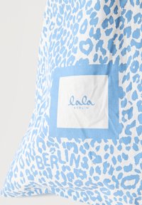 Ύφασμα με λευκό και μπλε σχέδιο λεοπάρ και τετράγωνη ετικέτα που γράφει "lala BERLIN" τοποθετημένη στο κέντρο του σχεδίου.