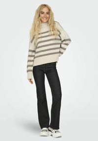 Pull crème avec des rayures grises, coupe décontractée, et poignets côtelés, associé à un jean foncé évasé et des baskets blanches avec des accents noirs.