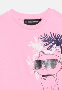 Ροζ παιδικό μπλουζάκι με καρτούν γάτα που φοράει μεγάλα γυαλιά ηλίου, γιακά με αστραπή και γραφικά με φοινικόδεντρο στο φόντο.