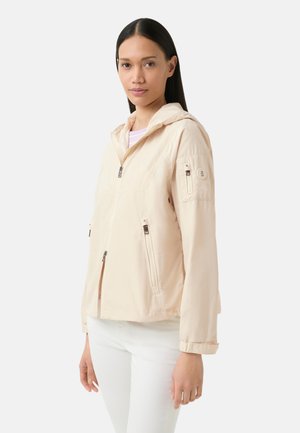 Veste à capuche beige clair avec fermeture éclair sur le devant, poches latérales et un patch sur la manche. Fabriquée en tissu lisse et léger.