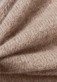 Weiches, hellbraunes Wollgewebe mit feiner Strickstruktur, das sanfte Wellen und eine leichte Flauschigkeit aufweist. Ideal für warme Kleidungsstücke oder Accessoires.